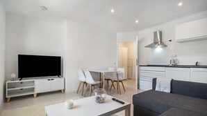 Ein modernes Wohnzimmer mit einem Flachbildfernseher, einem Esstisch mit Stühlen, einem grauen Sofa und einer Küchenzeile mit Schränken und Dunstabzugshaube.