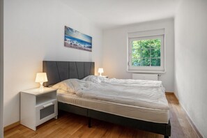 A bedroom with a bed, nightstands, a window, and a painting on the wall. - Apartment 'Whg 1.6 EG Rechts Hinten' with Private Terrace and Wi-Fi (Putbus)