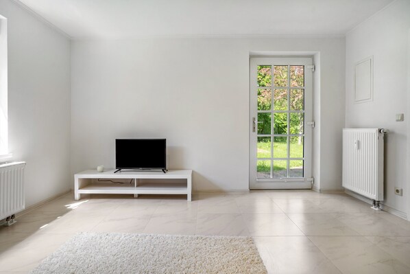 Una stanza con una TV bianca su un mobile, un termosifone bianco e una porta che dà all'esterno.