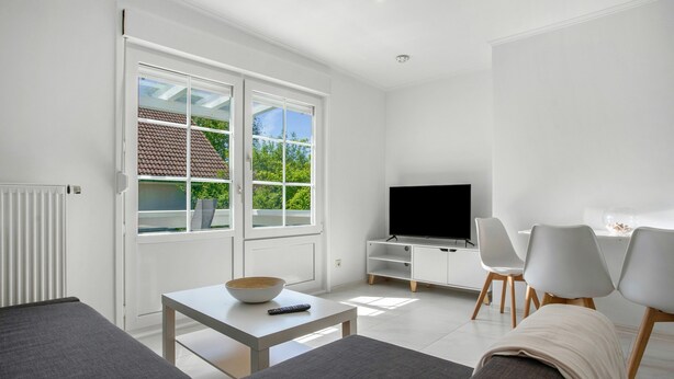 Uma sala de estar moderna com televisão, sofá e área de jantar.