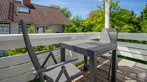 Um terraço com mesa e cadeiras, guarda-corpo branco e uma casa com telhado de cerâmica ao fundo.
