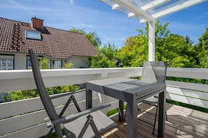 Um terraço com mesa e cadeiras, guarda-corpo branco e uma casa com telhado de cerâmica ao fundo.