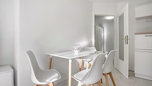 Uma área de refeições moderna com uma mesa e cadeiras brancas, um vaso de vidro e um armário branco.