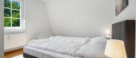 Un dormitorio con cama, lámpara de noche, ventana y un cuadro en la pared.