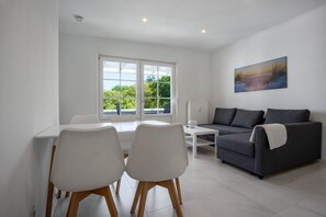 Una sala de estar moderna con una mesa de comedor blanca, dos sillas blancas, un sofá gris y un cuadro en la pared.