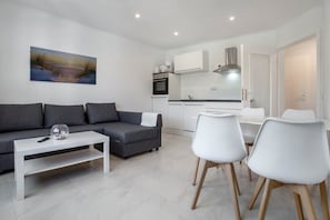 Uma sala de estar moderna com um sofá cinzento, uma mesa de centro branca e uma pintura de um pôr do sol.