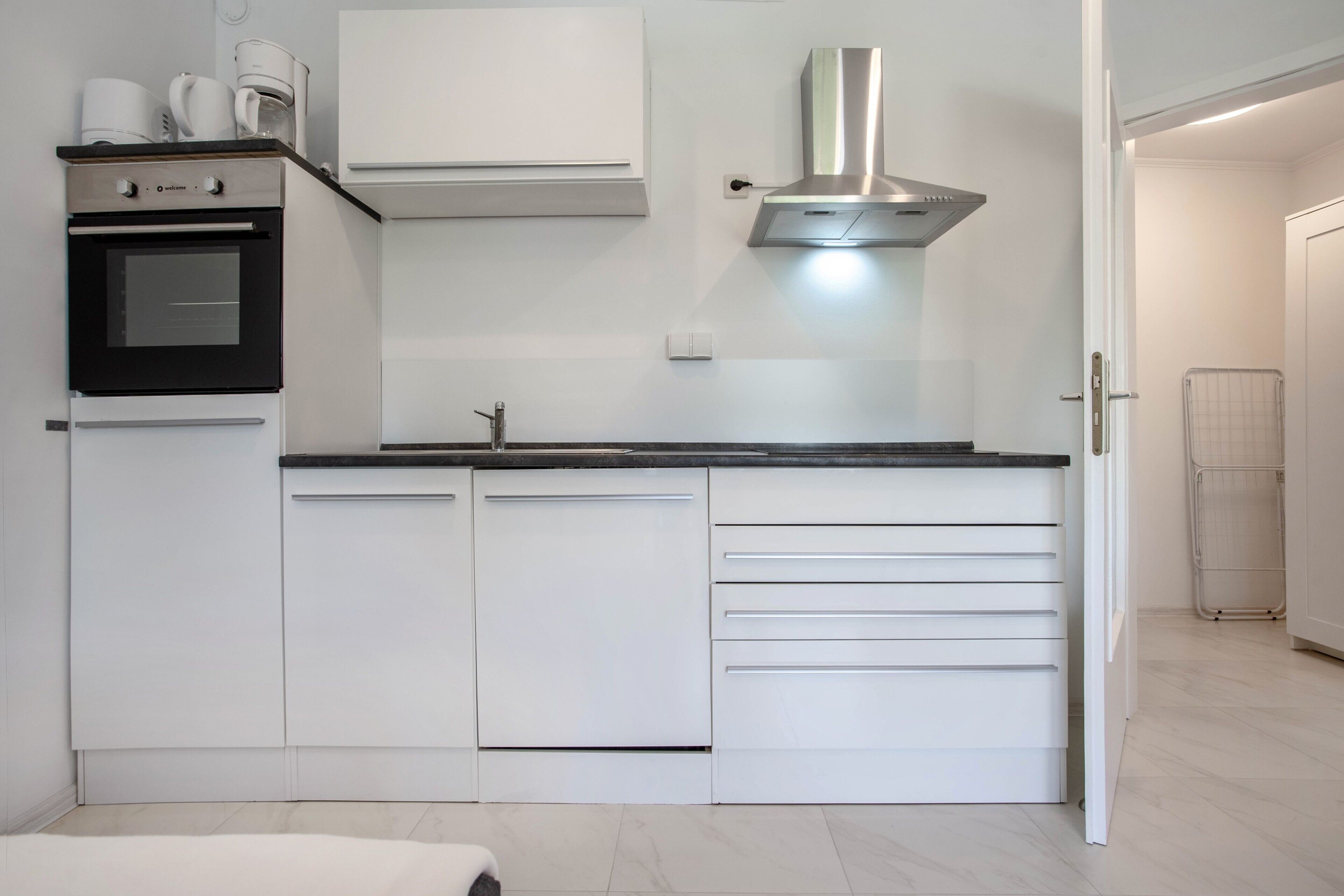 Une cuisine moderne avec des meubles blancs, une hotte en acier inoxydable et un four encastré.
