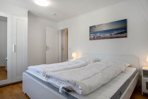 Quarto com cama, mesa de cabeceira, luminária na parede e uma porta.