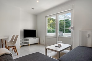 Uma sala de estar moderna com televisão de tela plana, área de jantar com cadeiras, sofá e mesa.