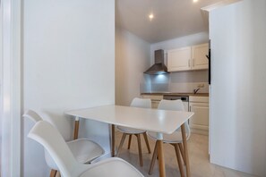 Una cucina compatta con mobili bianchi, una cappa in acciaio inossidabile e un tavolo da pranzo bianco con sedie.