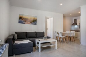 Een moderne woonkamer met een bank, salontafel en stoelen, een schilderij aan de muur en een keuken op de achtergrond.
