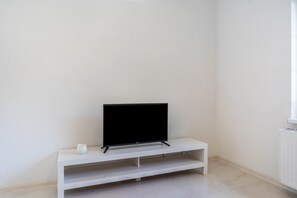 Un mueble blanco para televisor con un televisor de pantalla plana, un pequeño florero blanco y una estantería blanca.