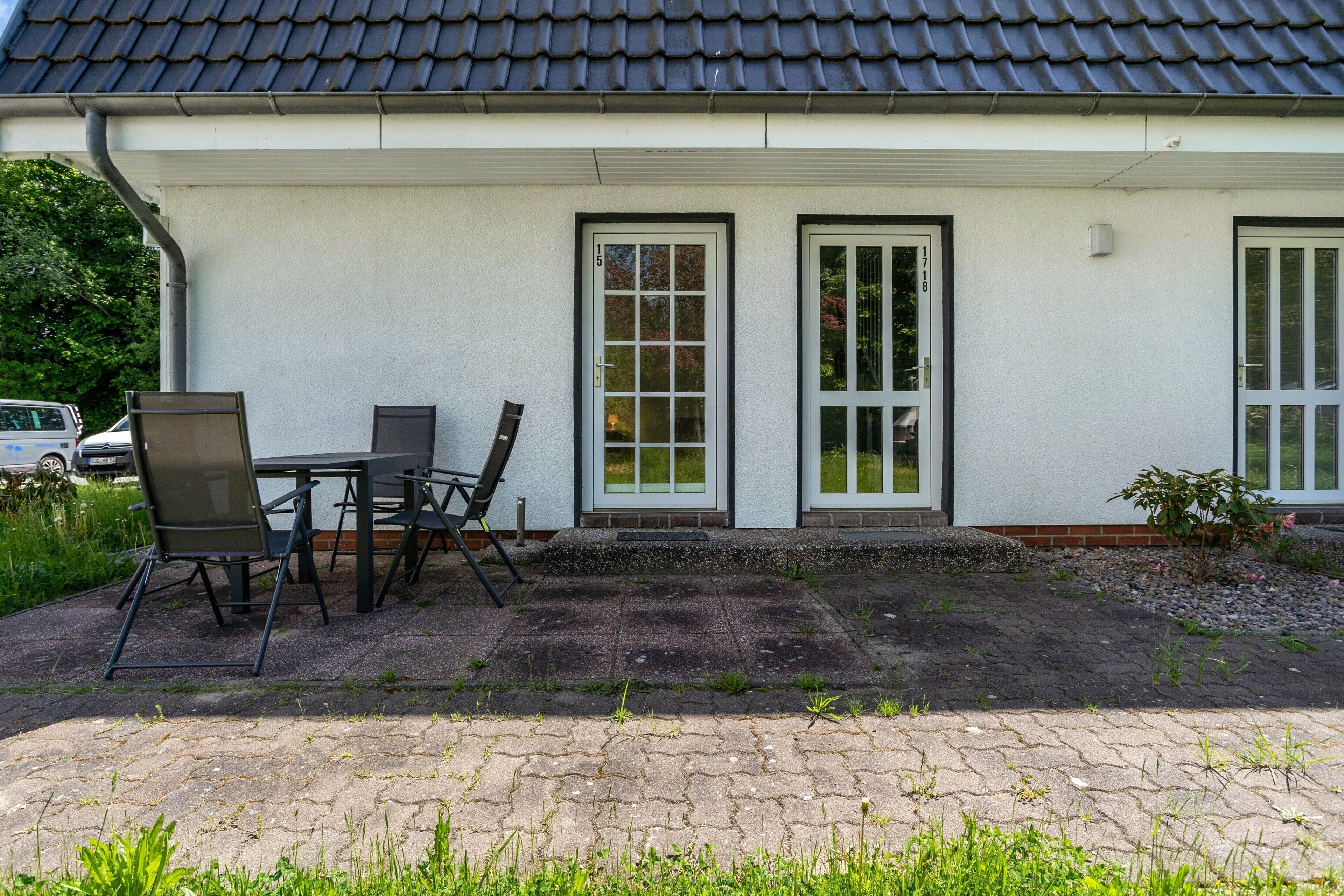 A building with a tiled roof, two doors, a table with chairs, and a paved area with grass.