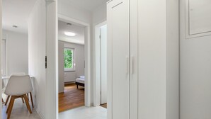 A hallway with white walls, a dining area with a white chair and table, a bedroom with a bed and window, and a white wardrobe. - Apartment 'Whg 2.4 1.OG Rechts Vorn' with Balcony (Putbus)