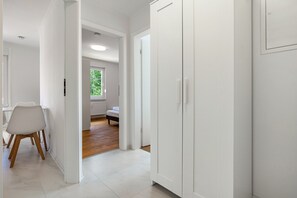 Een hal met witte muren, een eetgedeelte met een witte stoel en tafel, een slaapkamer met een bed en raam, en een witte garderobe.