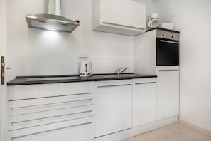 Une cuisine moderne avec des meubles blancs, une hotte de cuisinière en acier inoxydable, une machine à café et un grille-pain.