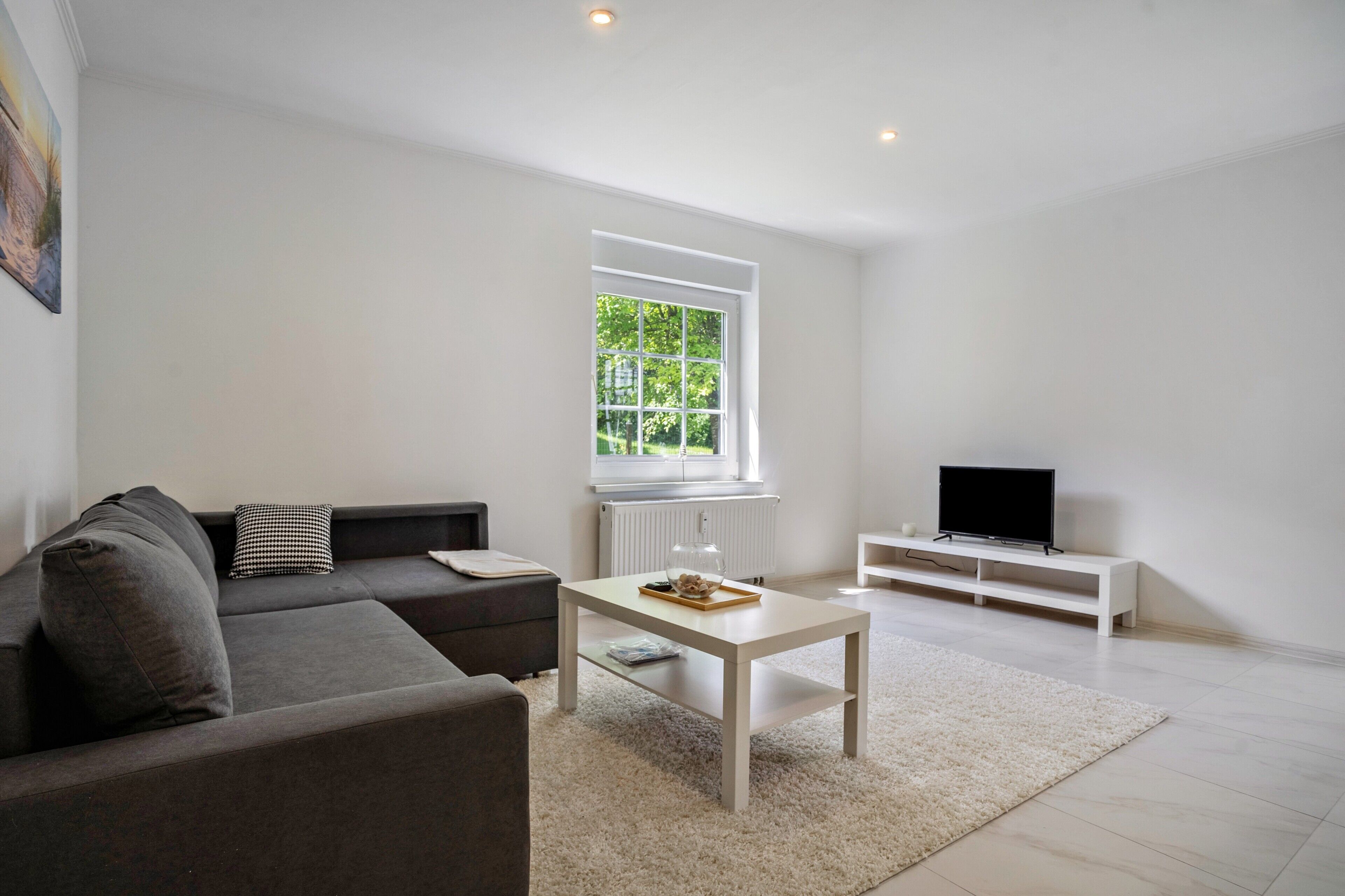Un salon moderne avec un canapé, une table basse, un meuble pour la télévision et une grande fenêtre.