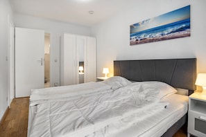 Una camera da letto con un letto, un comodino, una lampada a parete, un armadio e un quadro raffigurante una spiaggia.