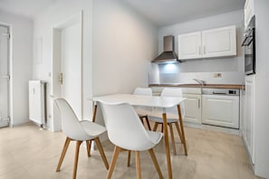 Una cucina moderna con mobili bianchi, una cappa aspirante in acciaio inossidabile e un'area pranzo con tavolo e sedie bianche.