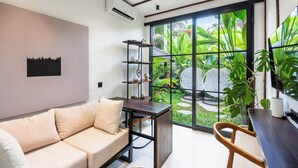 A modern living room with a sofa, a wooden table, and a large window with a view of greenery. - Villa Oasis (Ubud)