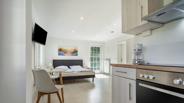 A modern kitchen with a built-in oven, a dining area with a table and chairs, a bed with a view, and a flat-screen TV mounted on the wall. - Apartment 'Whg 2.2 EG Rechts Vorn' with Private Terrace (Putbus)