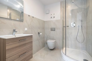Ein modernes Badezimmer mit einer begehbaren Glasdusche, einem weißen Waschbecken und einer Toilette.