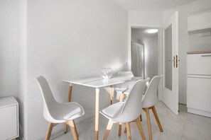 Uma área de refeições moderna com uma mesa e cadeiras brancas, um vaso de vidro e um armário branco.