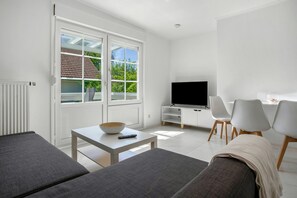 A modern living room with a TV, sofa, and dining area. - Apartment 'Whg 2.8 1.OG Rechts Hinten' with Balcony (Putbus)