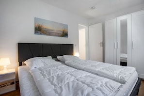 Una cama doble con cabecera, mesitas de noche con lámparas, un cuadro en la pared y un armario.