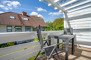 Un terrazza in legno con tavolo e sedie, una ringhiera bianca e una casa con tetto a tegole sullo sfondo.