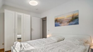Een slaapkamer met een bed, een witte inbouwkast en een schilderij van een zonsondergang.