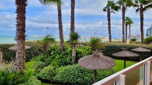 Un balcón con vistas a un jardín ajardinado, palmeras y un paisaje urbano distante.