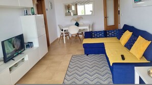 Una sala de estar con sofá, televisor y una zona de comedor con mesa y sillas.