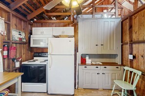 Una cocina compacta con paredes de madera, un refrigerador blanco, una estufa y una silla de madera.