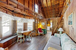 A rustic cabin interior with wooden walls, a dining area with a table and chairs, a sofa, and a staircase. - Town of Dewey Beach - 103 New Orleans St Unit B (Dewey Beach)