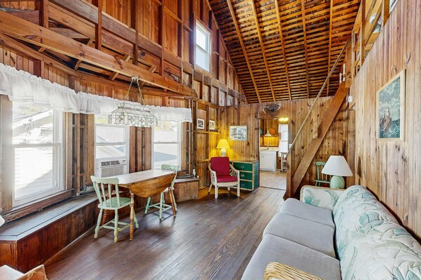 L’intérieur d’un chalet rustique, avec des murs en bois, un coin repas comprenant une table et des chaises, un canapé et un escalier.