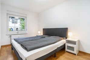 A bedroom with a bed, bedside tables, a window, and a radiator.