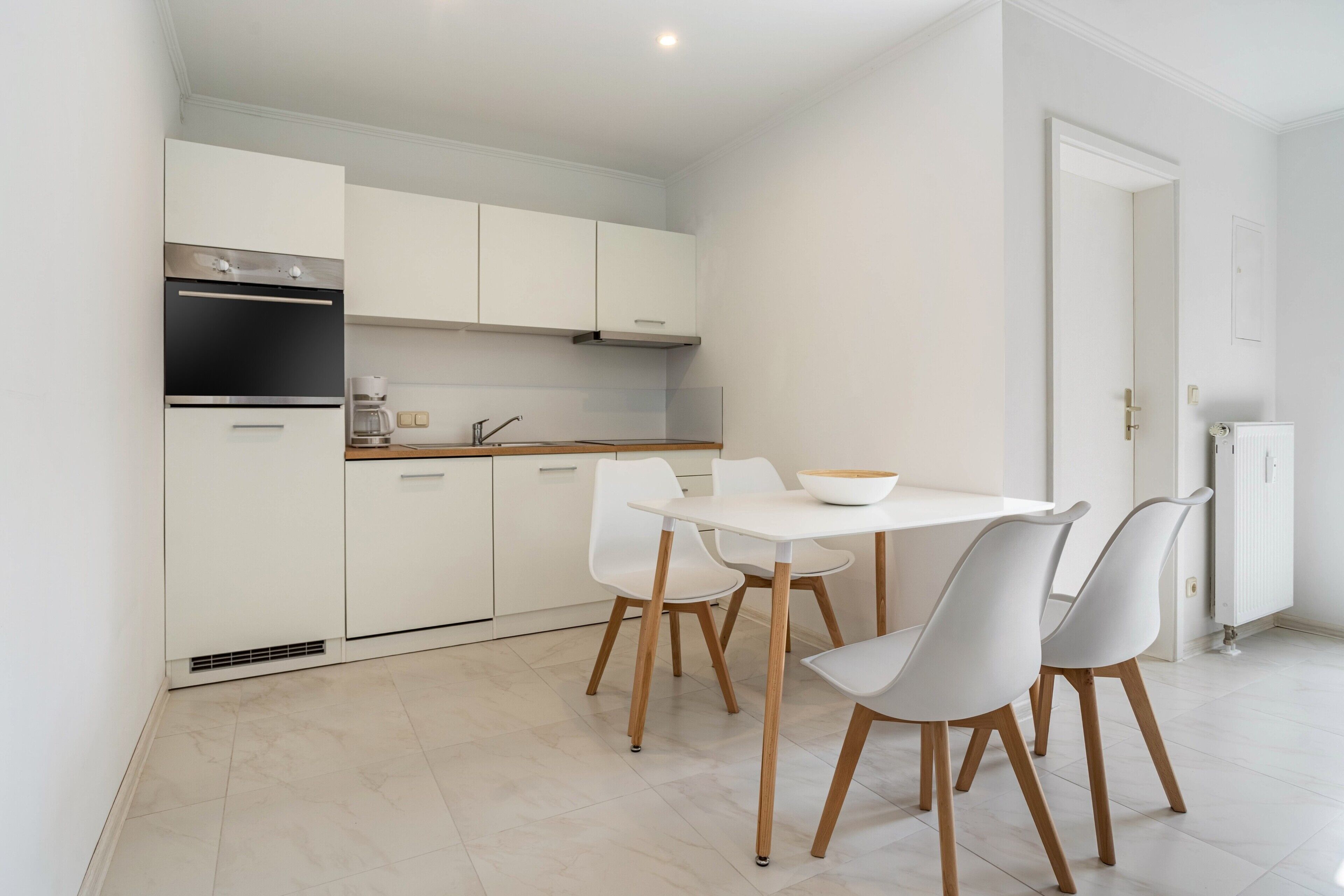 A modern kitchen with white cabinets, a built-in oven, and a dining area with a white table and chairs.