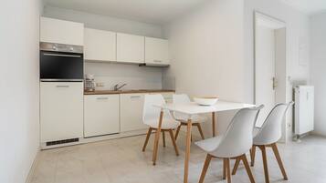 A modern kitchen with white cabinets, a built-in oven, and a dining area with a white table and chairs.
