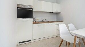 Una cocina moderna con armarios blancos, un horno de acero inoxidable, un fregadero y una zona de comedor con sillas blancas.