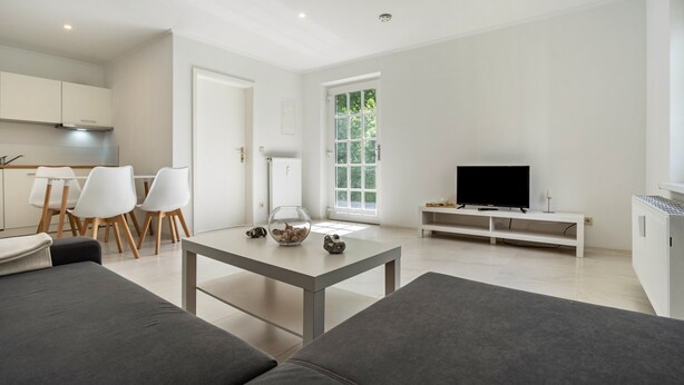 Una sala de estar moderna con un sofá, una mesa de centro, un televisor y un comedor con sillas y una mesa.