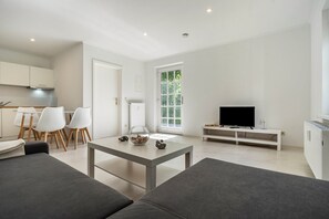 Un salon moderne comprenant un canapé, une table basse, un téléviseur et un coin repas avec des chaises et une table.