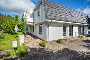 Een modern huis met twee verdiepingen, een grijs dak, witte buitenmuren en een klein voortuintje.