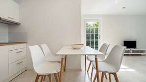 Una cocina moderna con armarios blancos, una mesa de comedor con cuatro sillas blancas y un televisor sobre un mueble blanco.