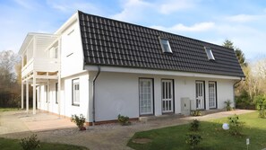 Une maison à deux étages, avec un toit en tuiles, des murs extérieurs blancs et un petit jardin à l’avant.