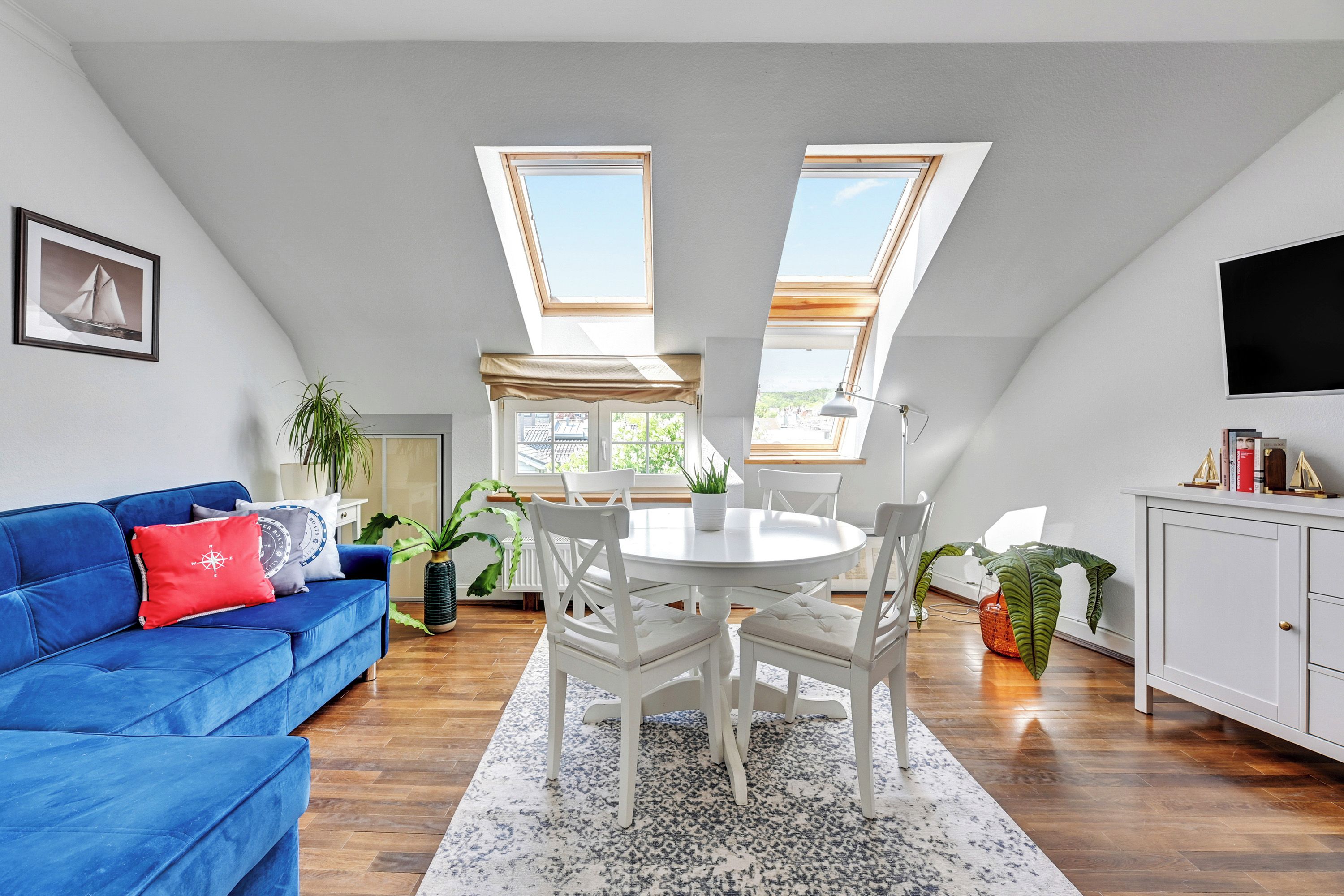 A modern loft with a dining area, a blue sofa, and a TV mounted on the wall.
