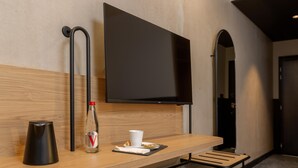 A hotel room with a wooden desk, a flat-screen TV, a bottle of water, a cup, and a tray with a napkin and a plate. - Tulip Hotels & Residences - Marseille Aubagne (Aubagne)