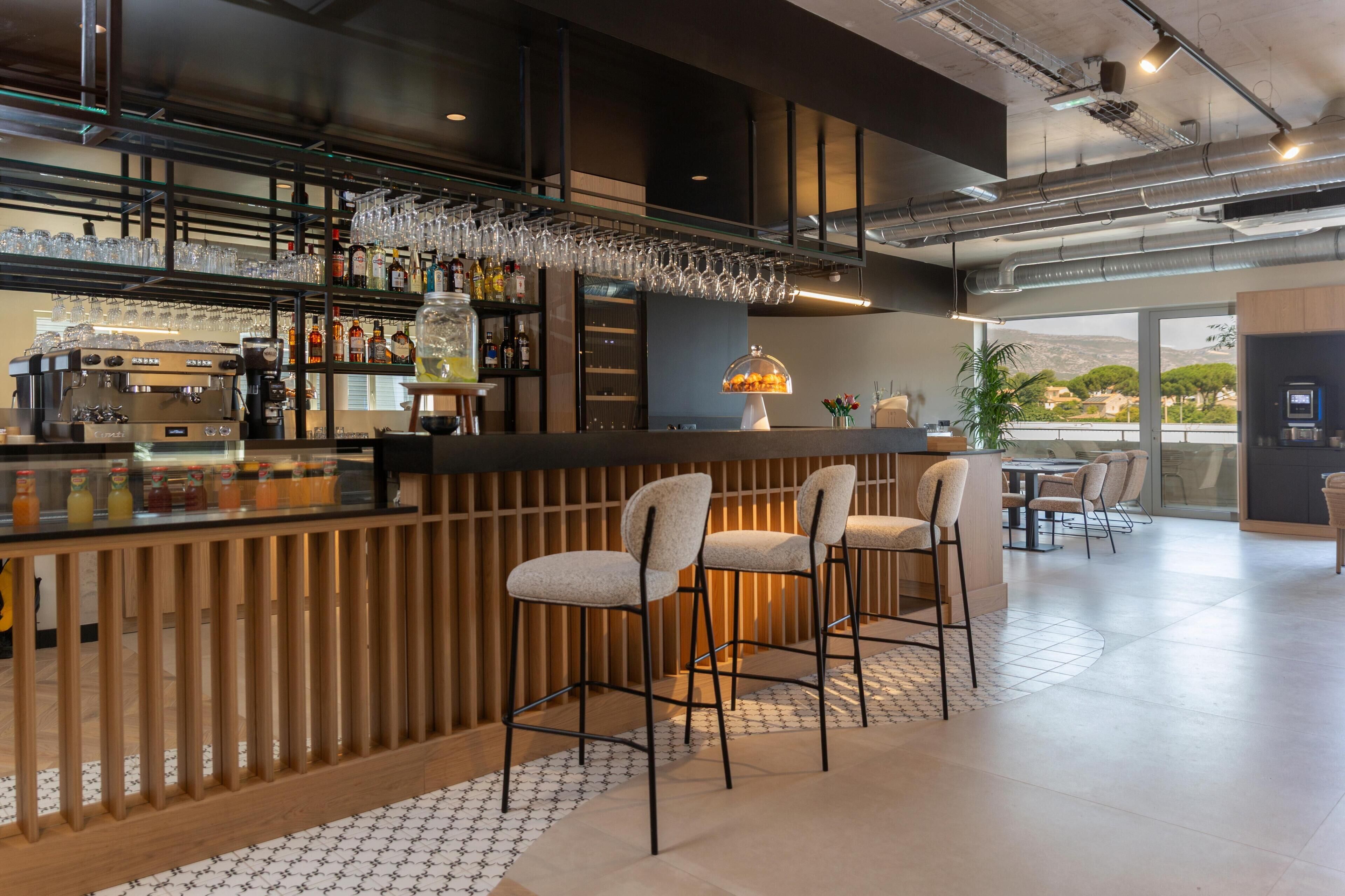 Een bar met een koffieapparaat, flessen op planken en glazen die hangen.