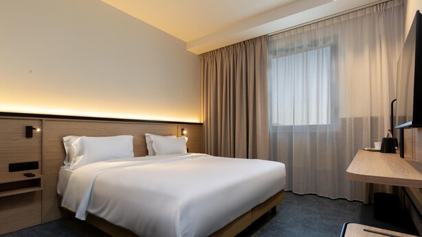 A hotel room with a bed, bedside tables, a desk, a chair, a TV, and a window with curtains. - Tulip Hotels & Residences - Marseille Aubagne (Aubagne)
