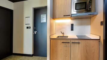 Een kleine keuken met een magnetron, een spoelbak en houten kastjes.